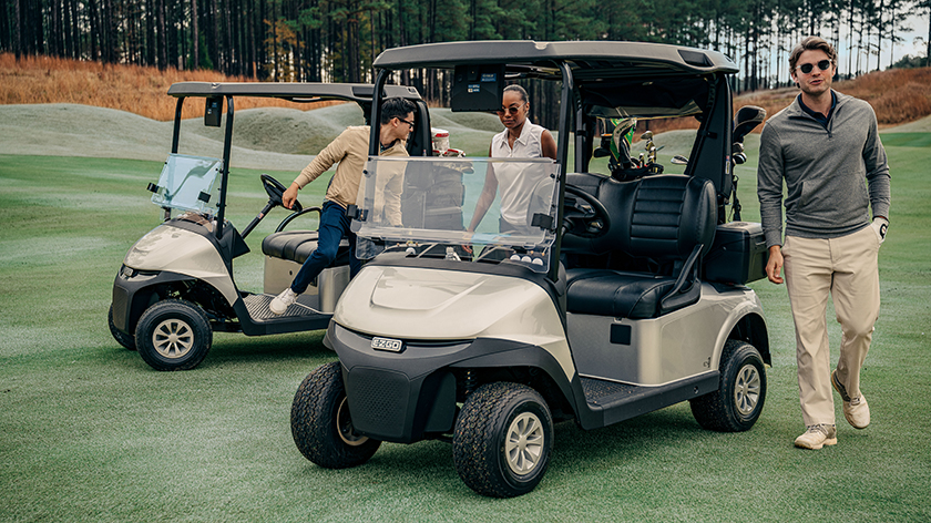 A group of golfers surrounding two E-Z-GO golf cart models.